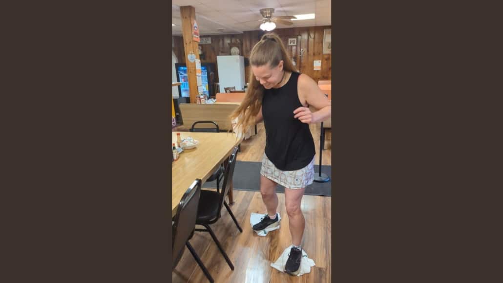 woman moping a restaurant floor with rags on her feet while laughing