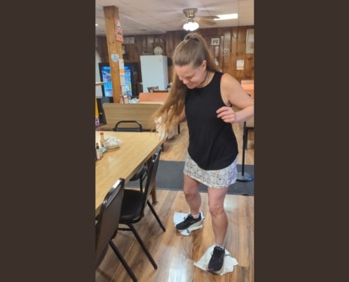 woman moping a restaurant floor with rags on her feet while laughing